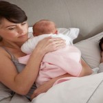 Mother Cuddling Newborn Baby In Bed At Home
