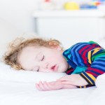 Adorable toddler girl taing a nap in a white sunny bedroom